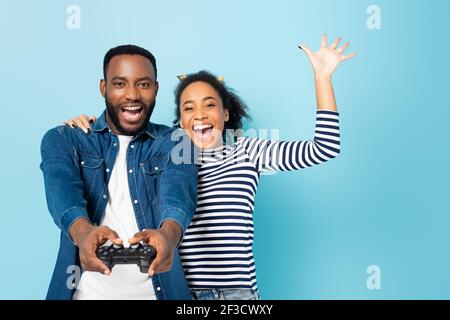 KIEW, UKRAINE - 23. OKTOBER 2020: Aufgeregt afroamerikanische Frau winkt Hand, während umarmt Mann Gaming auf blau Stockfoto