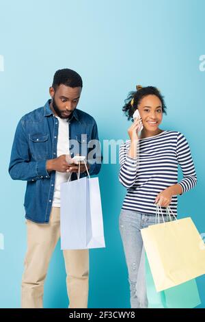 Schockiert afroamerikanischen Mann Messaging auf dem Smartphone in der Nähe glückliche Frau Im Gespräch auf Blau Stockfoto
