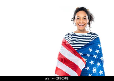 Fröhliche afroamerikanische Frau, eingewickelt in die usa-Flagge, lächelnd auf die Kamera isoliert auf weiß Stockfoto