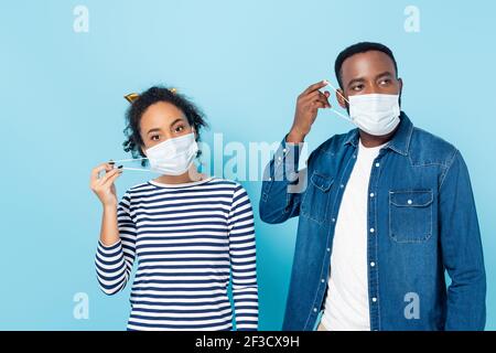 Junges afroamerikanisches Paar, das medizinische Masken auf Blau aufsetzt Stockfoto