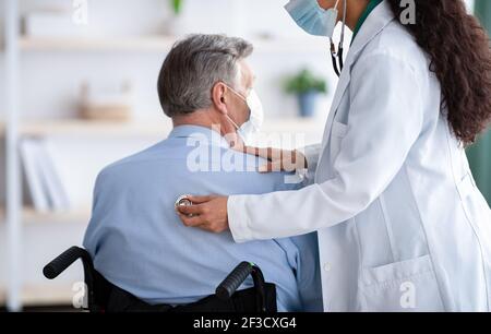 Leitender männlicher Patient im Rollstuhl, der an Atemwegserkrankungen leidet, mit Coronavirus, medizinische Fachkraft, die ihm hilft Stockfoto