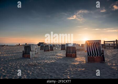 Gruppe von überdachten Korbliegen am Sandstrand während des Sonnenuntergangs. Strandausrüstung in Ferienanlagen. Sommerurlaub, Urlaub am Meer Konzept. Stockfoto