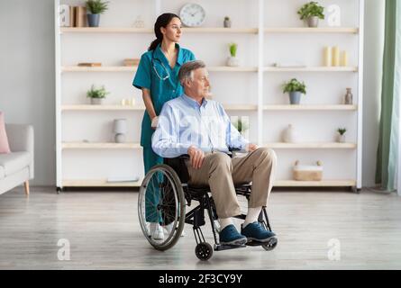 In voller Länge Porträt von älteren männlichen Patienten im Rollstuhl und Seine junge Pflegekraft im Altersheim Stockfoto