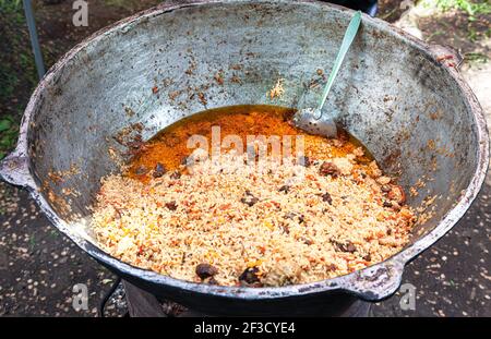 Kochen appetitlich traditionellen orientalischen Pilaf mit Fleisch in einem großen Kessel im Freien, Street Food Stockfoto