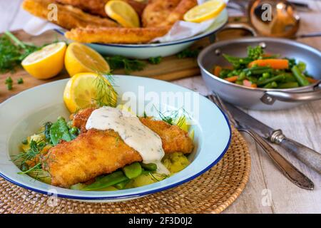 Fischgericht mit panierten Fisch, Gemüse, Kartoffeln und weißer Soße auf einem Teller Stockfoto