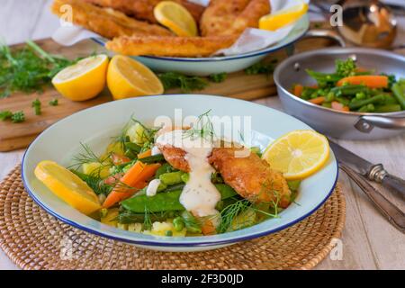 Fischabendessen mit panierten Fisch, Gemüse, Kartoffeln und Dillsoße auf einem Teller Stockfoto