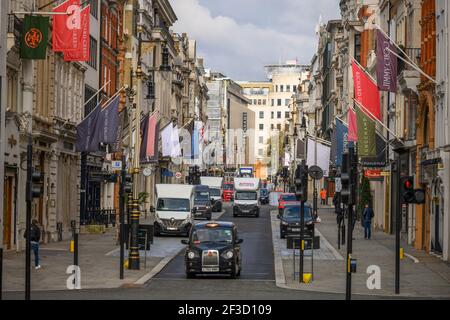 London, Großbritannien. 16. März 2021. Der Verkehr fließt durch die New Bond Street im Zentrum Londons, ohne Staus während der Sperre von Covid-19 im März 2021 und die Flaggen des Luxushändlers geben einen Eindruck von Normalität, aber alle Luxusgeschäfte und Galerien bleiben derzeit geschlossen und nur wenige Fußgänger sind in der Nähe. Der große Debenhams-Laden in der Oxford Street, im Zentrum von SHOT, hat nun dauerhaft geschlossen. Quelle: Malcolm Park/Alamy Live News. Stockfoto