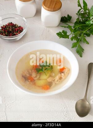 Transparente Fischsuppe mit Gemüse und Perkussion in einer weißen Schüssel auf einem weißen Teller. Gesunde Ernährung Konzept. Vertikale Ausrichtung. Stockfoto