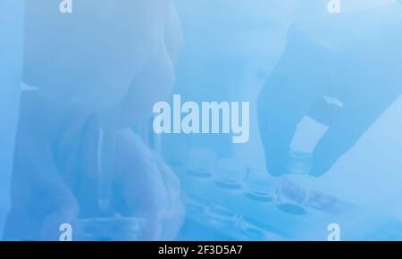 Wissenschaftliche Forschung - Hände von wissenschaftlichen Labortechniker Pipettieren in Forschungslabor. Blaue Handschuhen, die eine flüssige Probe im Glas entnehmen. Stockfoto