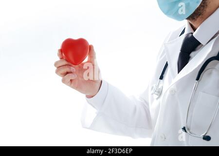 Arzt in einer Schutzmaske hält ein rotes Herz in seinen Händen. Stockfoto