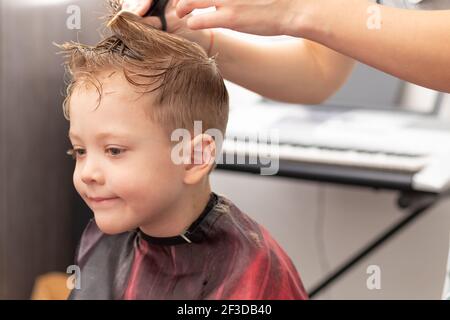 Fürsorgliche weibliche Hände einer Mutter mit Kamm und Schere machen einen modischen Haarschnitt für ihren Sohn zu Hause während der zweiten Sperre. Selektiver Fokus Stockfoto