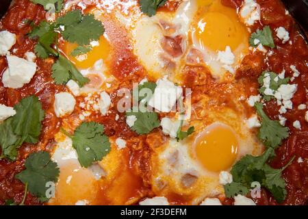 Ein köstlicher Topf mit Shakshuka mit Avocado und Harissa Eiern Kochen in einer großen Pfanne Stockfoto