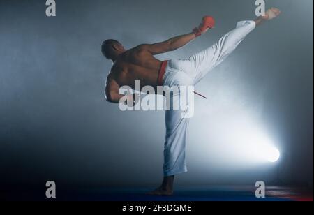 Männliche Karate Kämpfer Durchführung Kick auf dunklem Hintergrund in der Turnhalle isoliert Stockfoto