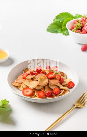 Sommerfrühstück mit winzigen Mini-Pfannkuchen und frischer Erdbeere auf weißem Tisch. Nahaufnahme. Vertikales Format. Stockfoto