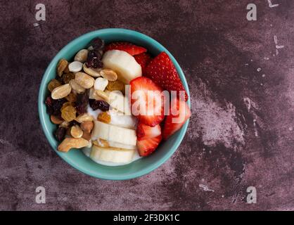 Draufsicht auf eine Schüssel mit schlichtem griechischen Joghurt-Süßigkeitenpfad, der Bananen und Erdbeeren auf einer Marron-Tischplatte vermischt. Stockfoto