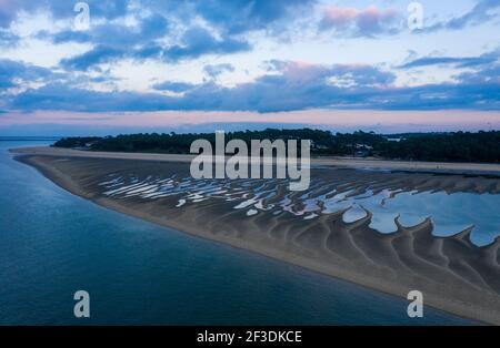 Drohnenblick auf den Sandstrand bei Ebbe. Große Wasserbecken, die von Sanddeichen zurückgehalten werden. Rosafarbener Himmel mit Wolken nach Sonnenuntergang. Stockfoto