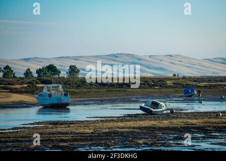 Boote, die bei Ebbe auf sandigen Boden festgemacht wurden. Küstenlandschaft mit Bäumen und Hügeln im Hintergrund. Stockfoto