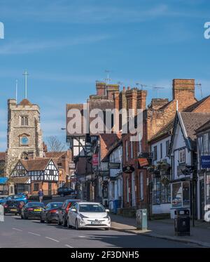 Pinner Village High Street mit der mittelalterlichen Bergkirche St. John the Baptist Parish Church, Geschäften, geparkten Autos und einem Mann, der auf dem Bürgersteig läuft Stockfoto