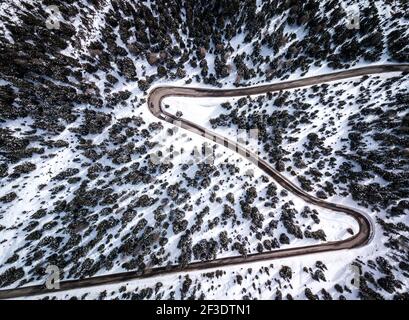Luftaufnahme auf der Straße zum Bergpass durch scharfe Kurven. Serpentinen in der Winterlandschaft von Sonnenschein beleuchtet. Stockfoto