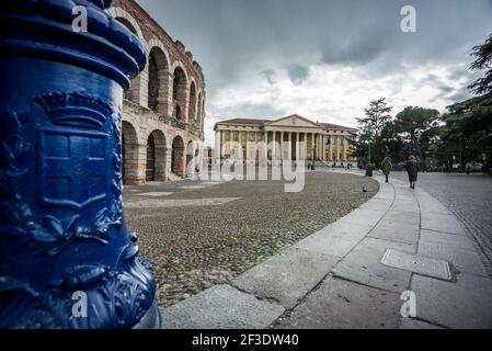 Weitwinkelansicht mehrerer Menschen, die durch das historische Stadtzentrum laufen. Zwei Reihen von Bögen in der Wand des römischen Amphitheaters. Stockfoto