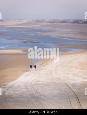 Luftaufnahme von zwei Personen, die an der Küste spazieren. In der Nebensaison nicht identifizierbare Personen am Sandstrand. Stockfoto