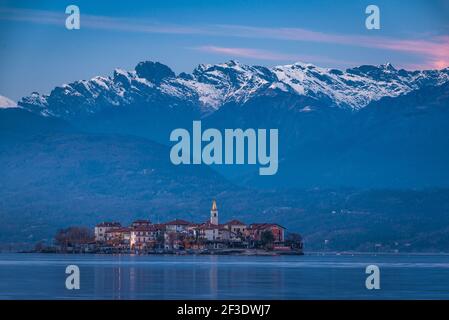 Blick am frühen Morgen auf die Kirche und die Häuser auf der Insel, die vom See umgeben ist. Schneebedeckten Bergrücken im Hintergrund. Stockfoto