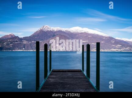 Panoramablick auf den schneebedeckten Bergrücken. Hölzerner Aussichtspunkt über der Wasseroberfläche des Sees im Vordergrund. Stockfoto