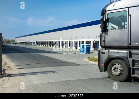 Beschnittene Ansicht des LKWs, der den Logistikpark betreten hat. Kabine des Staplers, der vor der Schranke steht. Reihe von Docks in der Hallenwand. Transport- und Logistikkonzept. Stockfoto