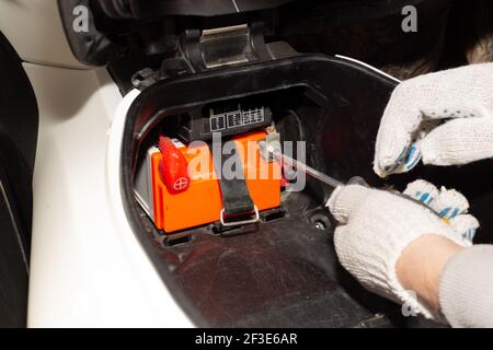 Austauschen der Motorradbatterie. Ein Automechaniker in einem Autodienst verwendet einen Schraubendreher, um die Batterie vom Motorrad zu entfernen, um sie zu laden oder zu ersetzen Stockfoto