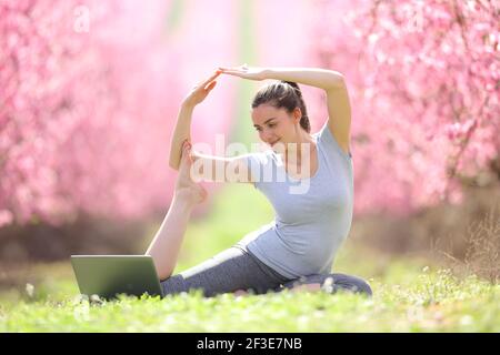 Zufriedene Frau tun Yoga-Übungen beobachten Video-Tutorial auf Laptop Im Freien in einem rosa blühenden Feld Stockfoto