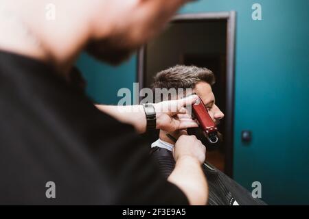 Mann, der im Friseursalon Haare schneidet, Nahaufnahme des Friseurs mit dem Haarschneider, um die Haare des männlichen Kunden zu schneiden. Stockfoto
