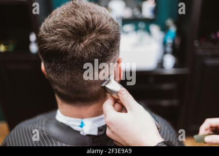 Männlicher Haarschnitt, Rückansicht des Kopfes des Kunden, während der Friseur schneidet die Haare mit Haarschneider, Nahaufnahme Stockfoto