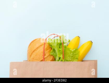 Papiertüte mit Lebensmitteln: Grüne Blätter von Salat, Brot und Banane. Layout auf blauem Hintergrund, Draufsicht Stockfoto