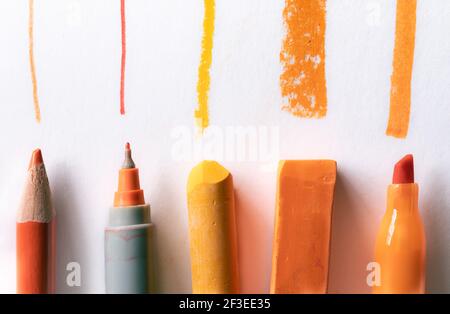 Orangefarbener Bleistift, Stift, Pastell und Markierungslinien auf weißem Hintergrund Stockfoto