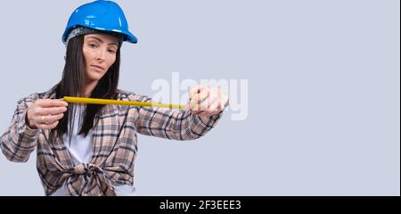 Banner, Langformat. Fokussierte Brünette Frau in Harthut mit Maßband auf weißem Hintergrund mit leerem Raum. Stockfoto