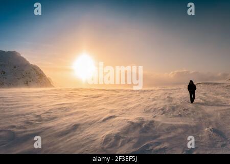 Panoramafotor des großen Sonnenuntergangs Halo in den Winterbergen, starker Schneewirbel. Eine Person in warmen schwarzen Schneemobil Overall und Schutzbrille läuft gegen s Stockfoto