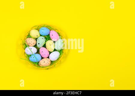 Bunte Ostereier in einer Schale auf gelbem Hintergrund. Platz für eine Inschrift. Blick von oben. Ostern. Stockfoto