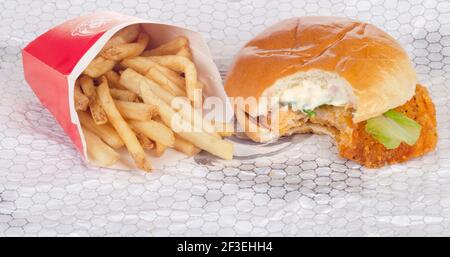 Wendy's Spicy Chicken Sandwich mit Biss auf Wrapper mit genommen Pommes Frites, auch Chips genannt Stockfoto