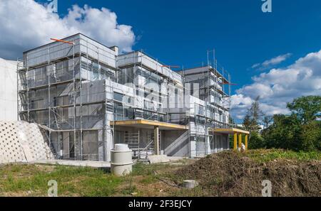 Neues Wohnhaus außen im Bau. Baustelle. Sommerlicher blauer Himmel. Moderne Apartments mit unvollendeter Fassade und Metallrohrgerüst. Stockfoto