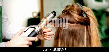 Rückansicht der weiblichen Friseurhände Locken Frauenhaare mit Lockenstab in einem Friseursalon Stockfoto