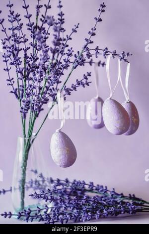 Osterkomposition mit Lavendelblüten in einer Glasvase und Lila Eier Stockfoto