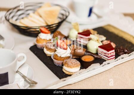 Board mit verschiedenen leckeren kleinen Kuchen zum Frühstück platziert auf Tablett im Hotelzimmer Stockfoto