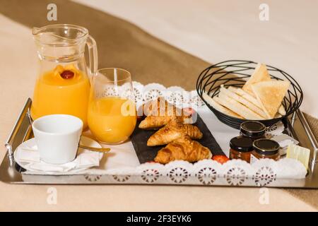 Metalltablett mit leckeren Frühstücksgebäck und frischem Orangensaft Auf dem Bett im Hotelzimmer platziert Stockfoto