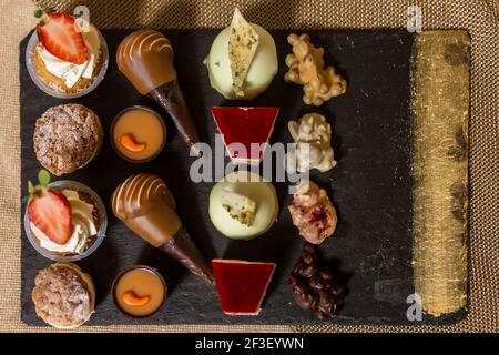 Von oben Set von verschiedenen schmackhaften Desserts auf schwarz serviert Brett mit goldenem Streifen im Hotelzimmer am Morgen Stockfoto