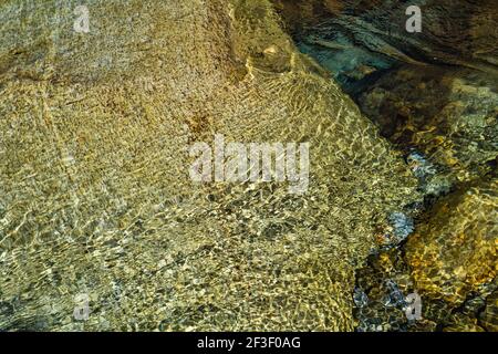 Große und kleine Steine unter kristallklarem Flusswasser.Stein und Wasser Hintergrund.Wasser Textur.Sommer Hintergrund.schöne Natur Hintergrund. Stockfoto