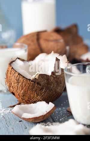 Kokosnusshälften und Stücke mit Glas Kokosmilch auf blauem Naturholzhintergrund. Stockfoto