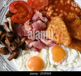 Traditionelles englisches Frühstück - Teller mit Spiegeleiern, Bohnen, Pilzen, Speck, Kartoffelrösti und Tomaten Stockfoto