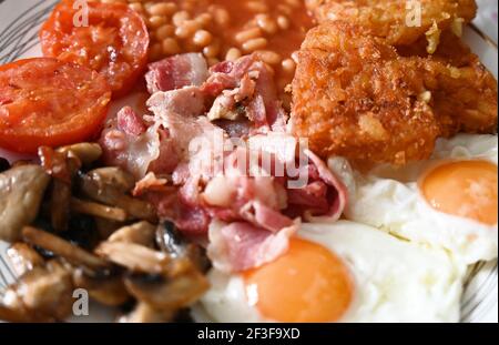 Traditionelles englisches Frühstück - Teller mit Spiegeleiern, Bohnen, Pilzen, Speck, Kartoffelrösti und Tomaten Stockfoto