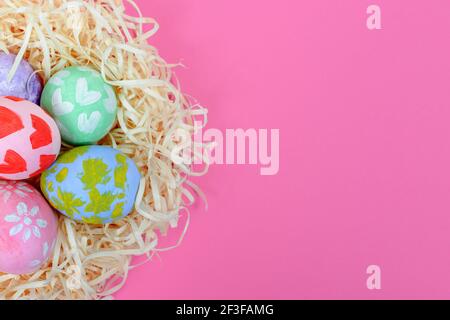 Nahaufnahme von bunten handgefertigten bemalten Ostereiern im Nest auf einem rosa Hintergrund. Eier von einem kleinen Kind gemalt. Draufsicht, Platz für Text Stockfoto