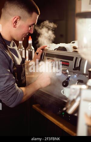 Lächelnder Barista mit professioneller Kaffeemaschine, der seine Arbeit genießt Cafe Verbesserung der Fähigkeiten der Herstellung von Cappuccino Stockfoto